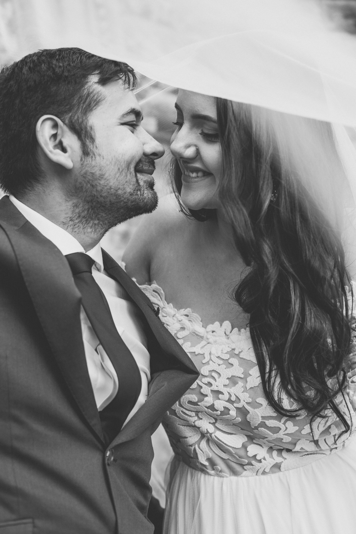 Black and white intimate wedding photo showing joyful couple sharing a romantic moment in lace dress and suit.