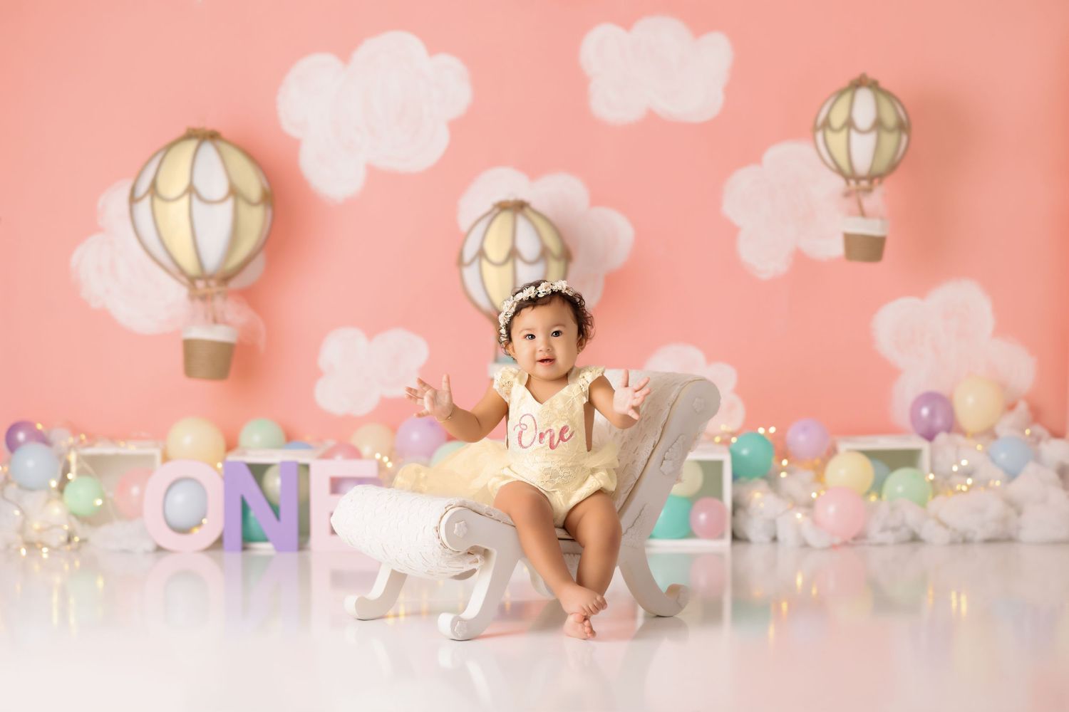 Delicate first birthday setup with hot air balloon decor, clouds, and pink backdrop for a magical celebration.