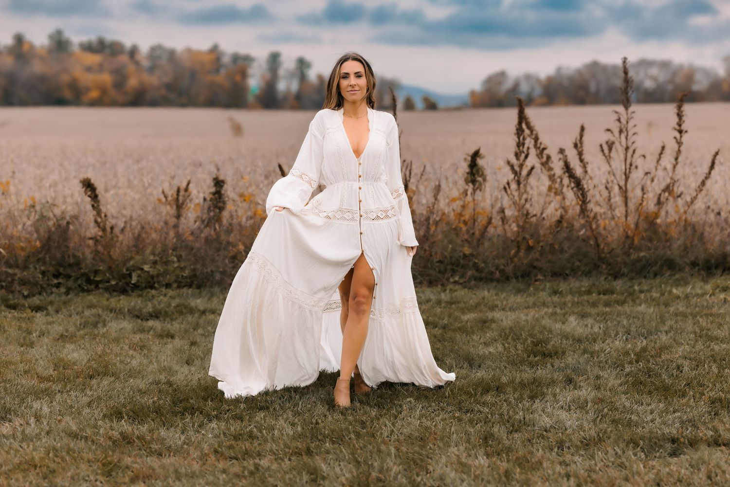 Woman in flowing white dress twirling in an autumn field at sunset.