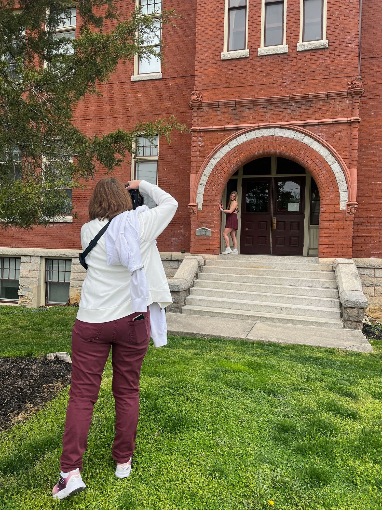 Person photographing red brick building entrance with arched doorway on college campus.