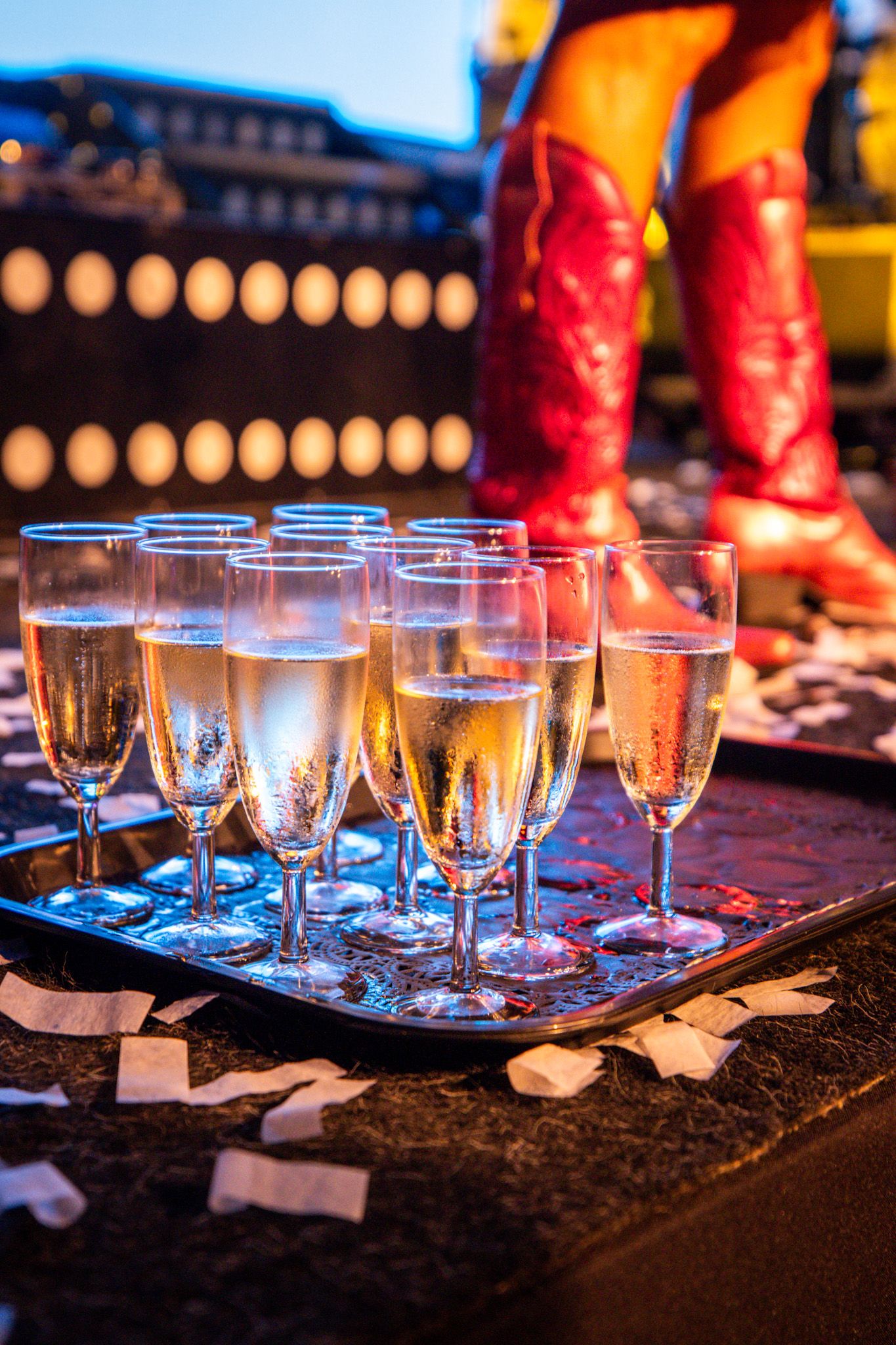 Een dienblad op een podium met champagneglazen en roze laarzen op de achtergrond.