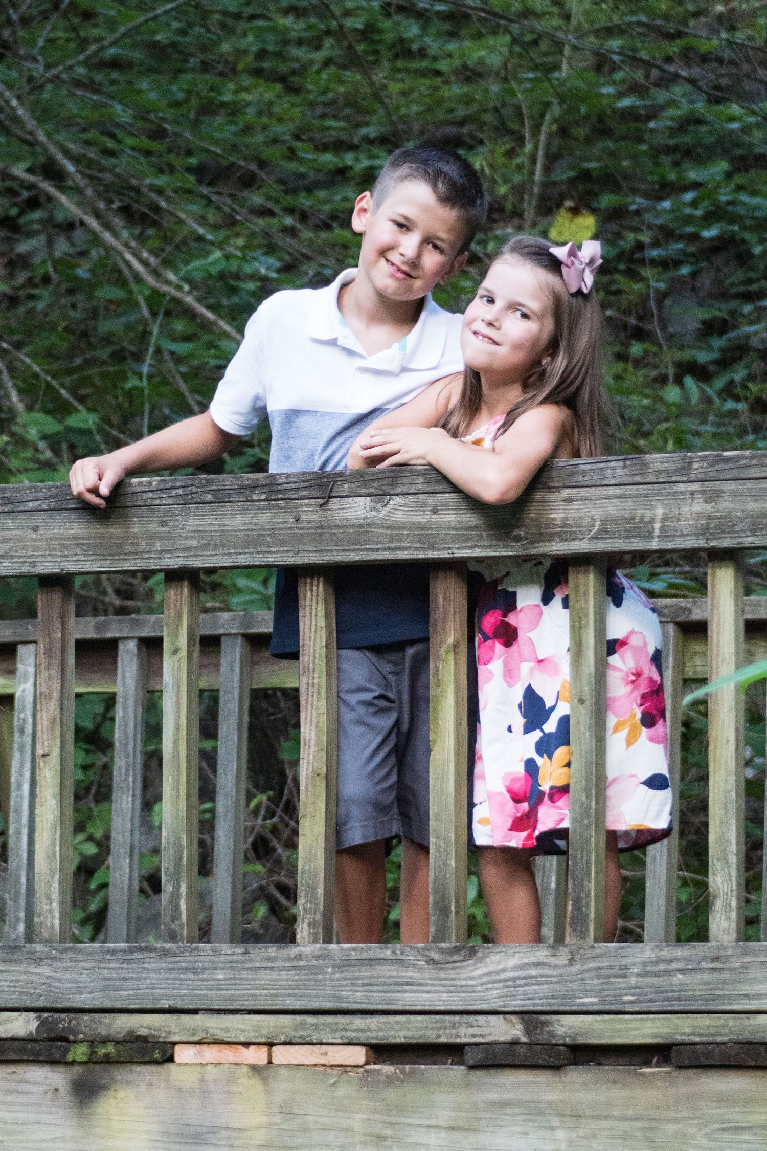Two young people lean on a wooden railing during an outdoor photo session.
