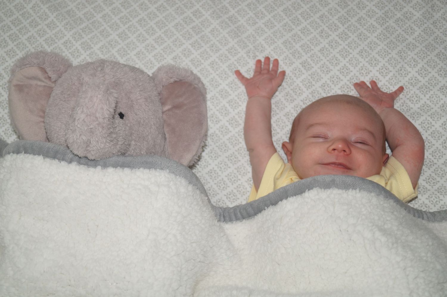 Baby lying on light colored textured blanket with hands raised.