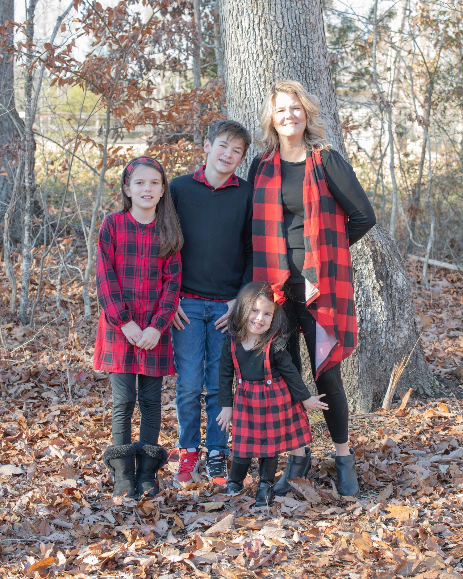 Family group wearing coordinating red buffalo plaid outfits poses in autumn forest setting.