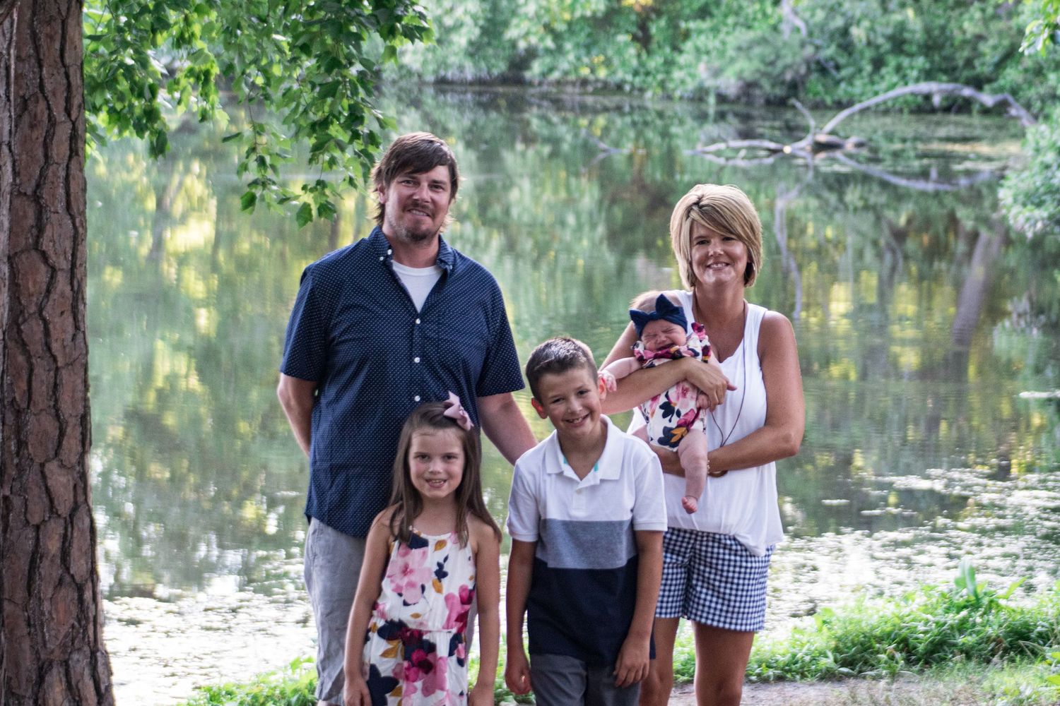 A family poses together by a tranquil pond on a sunny summer day.