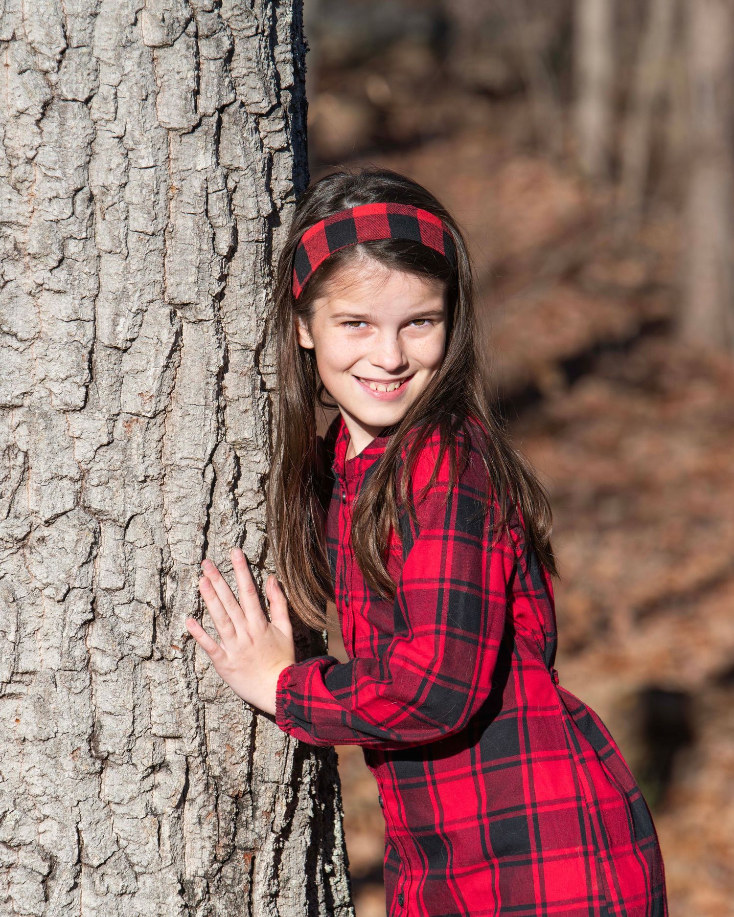 Person in red plaid leaning against large tree trunk in autumn forest setting.
