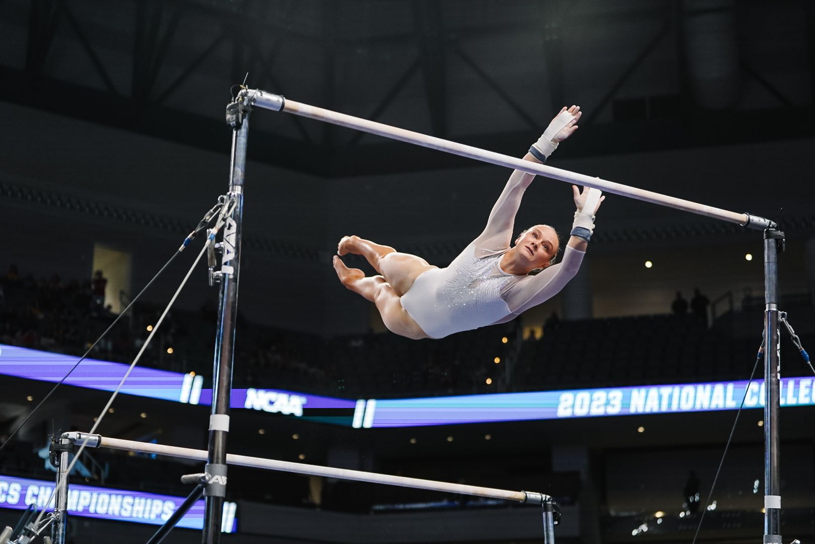 Athletic performance on uneven bars showing complex gymnastics skills in competition setting.