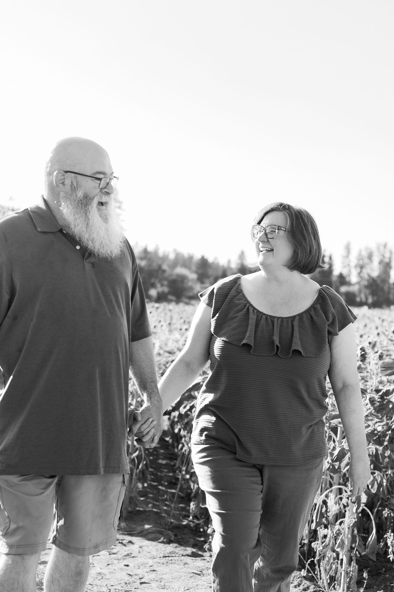 A couple strolls together through a sunlit field holding hands.