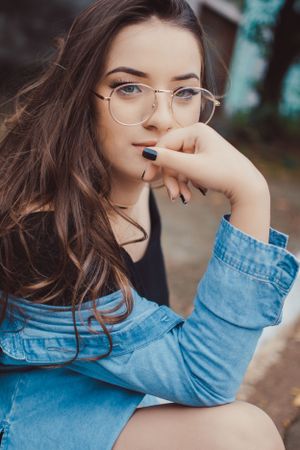 Close-up fashion portrait showcasing round glasses and denim jacket details.