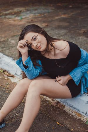 Casual street style pose featuring denim jacket and dark outfit on pavement.