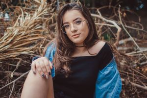 Natural light portrait featuring denim jacket and glasses against dried foliage backdrop.
