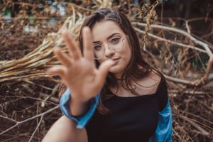 Portrait showing glasses and raised hand against a natural backdrop with blurred branches.