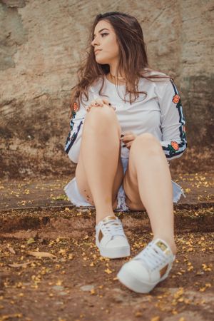 Relaxed outdoor portrait with white sneakers and decorative sleeve details.