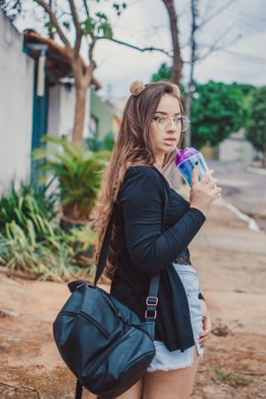 A casual outdoor portrait showing a black cardigan, denim shorts, and backpack against a garden backdrop.
