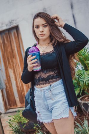 Stylish outfit with black lace top, cardigan and denim shorts while holding a colorful drink.
