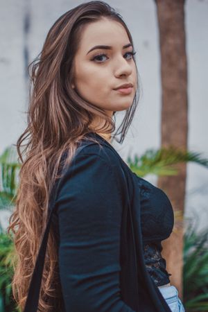 Long-haired portrait in black cardigan and lace top against tropical foliage.