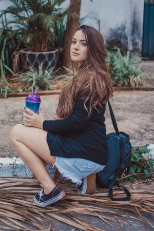 Casual lifestyle shot with backpack and colorful drink while sitting on wooden surface outdoors.
