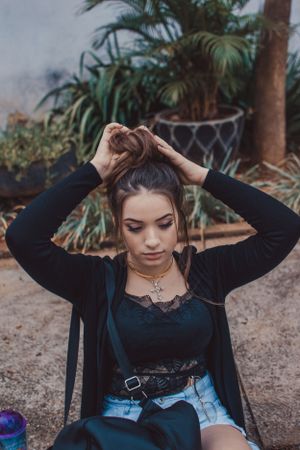 Casual portrait outdoors styling hair while wearing black top and denim shorts.