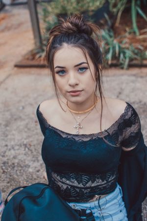 Fashion portrait featuring lace top and cross necklace with natural garden backdrop.