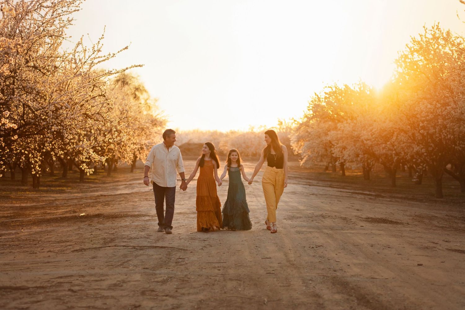 Family walking together through orchard at golden sunset on dirt path.