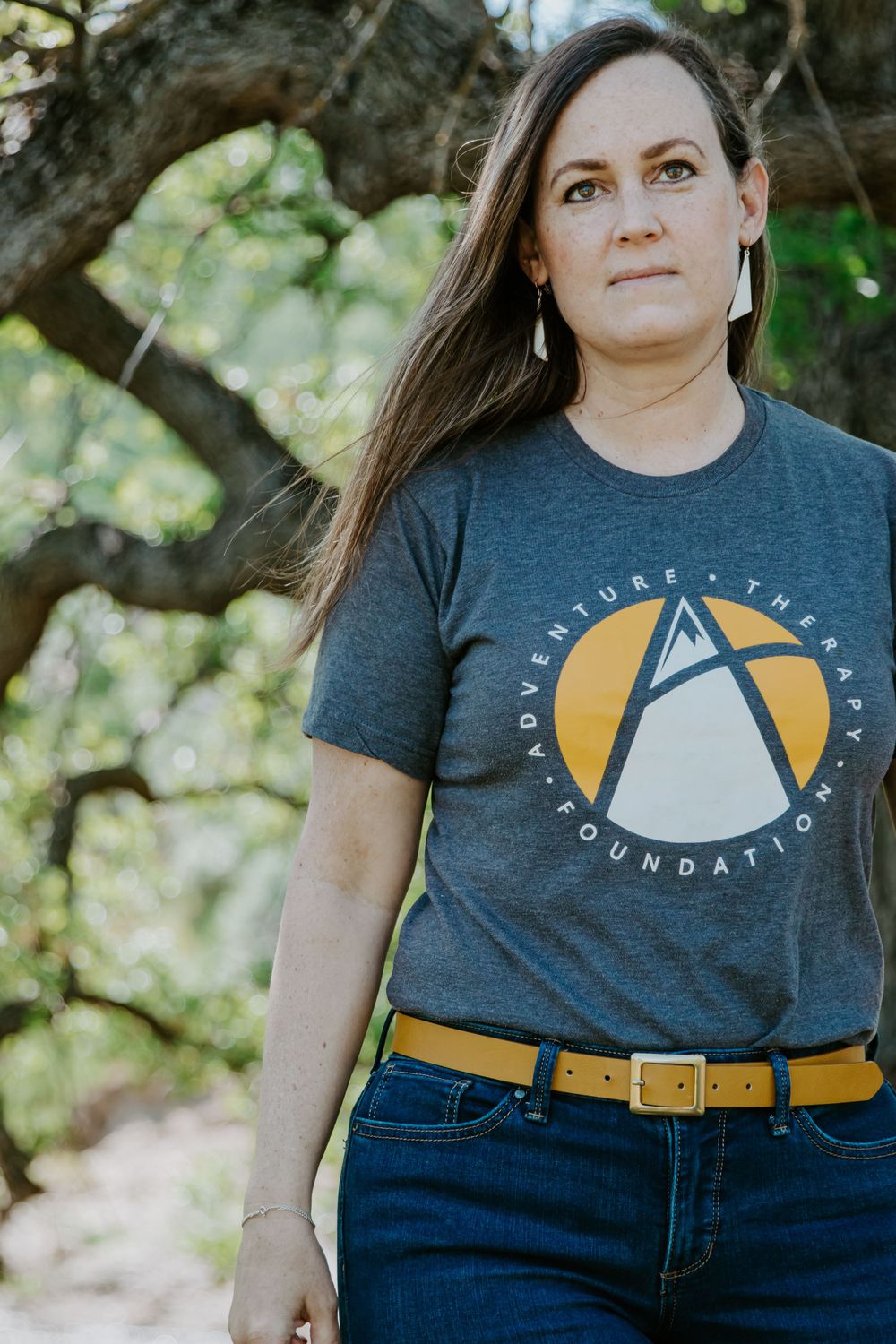 A person wearing a navy t-shirt with a yellow logo stands outdoors against a natural backdrop.