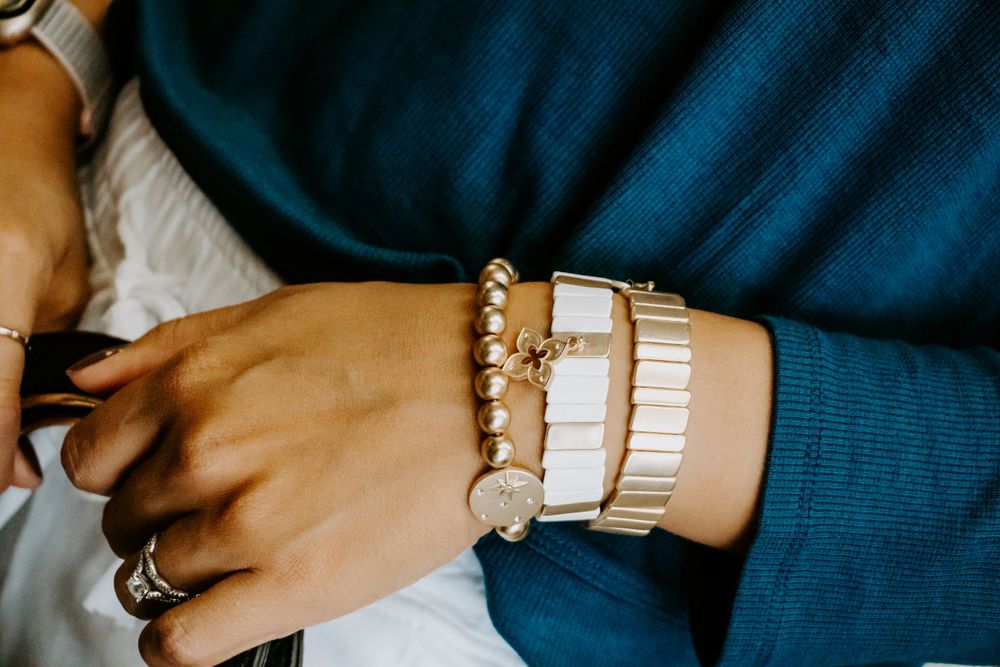 Stack of trendy white beaded bracelets shown on wrist with teal sweater sleeve.