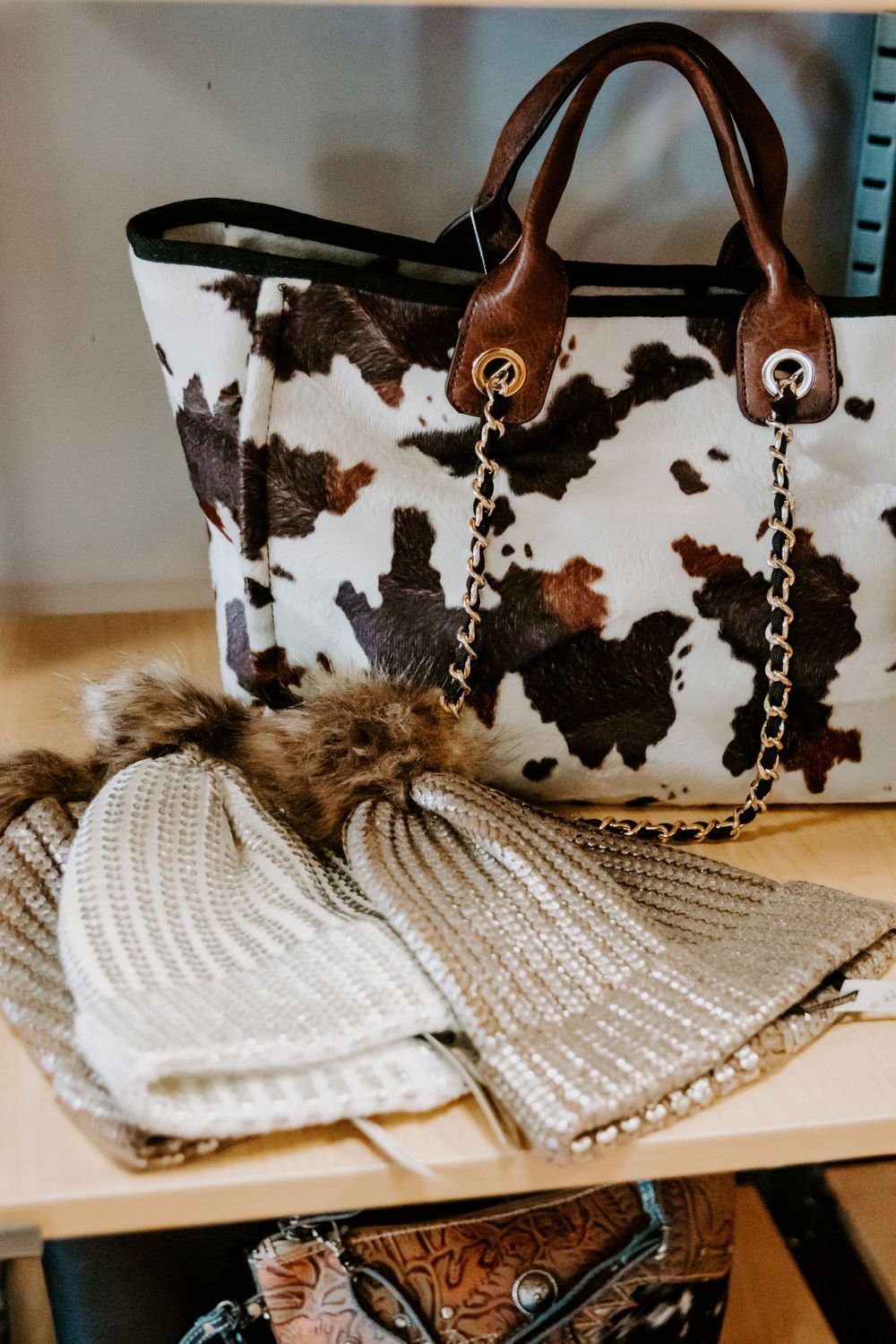 Cowhide print handbag with chain details displayed next to knit accessories.