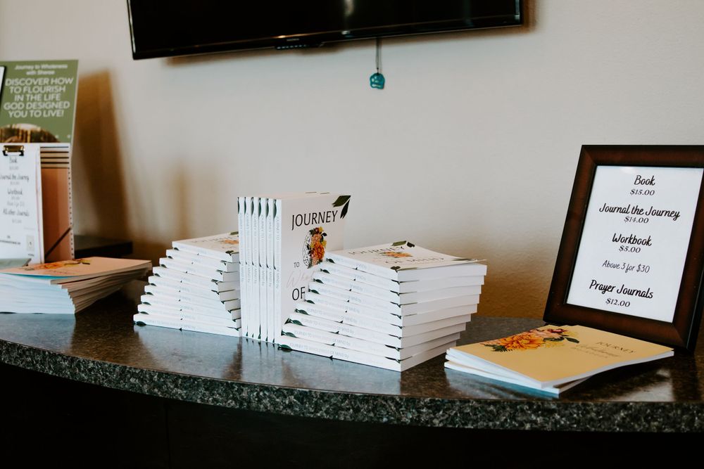 Stack of white books displayed on a dark granite counter at a promotional event.