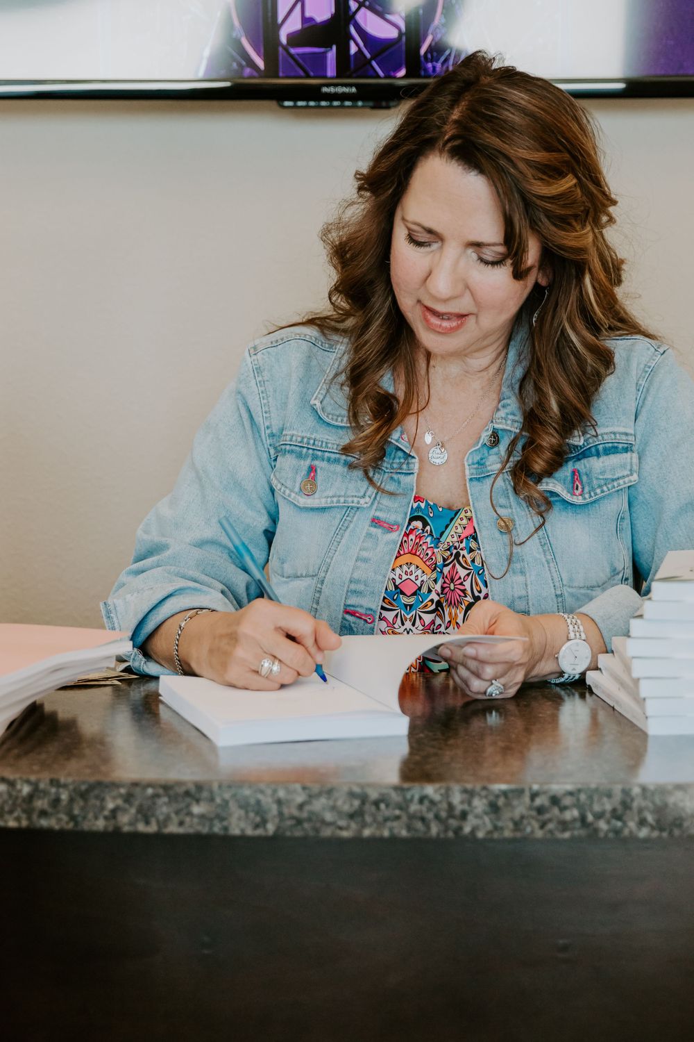 Person writing in a notebook while sitting at a dark counter wearing a denim jacket.