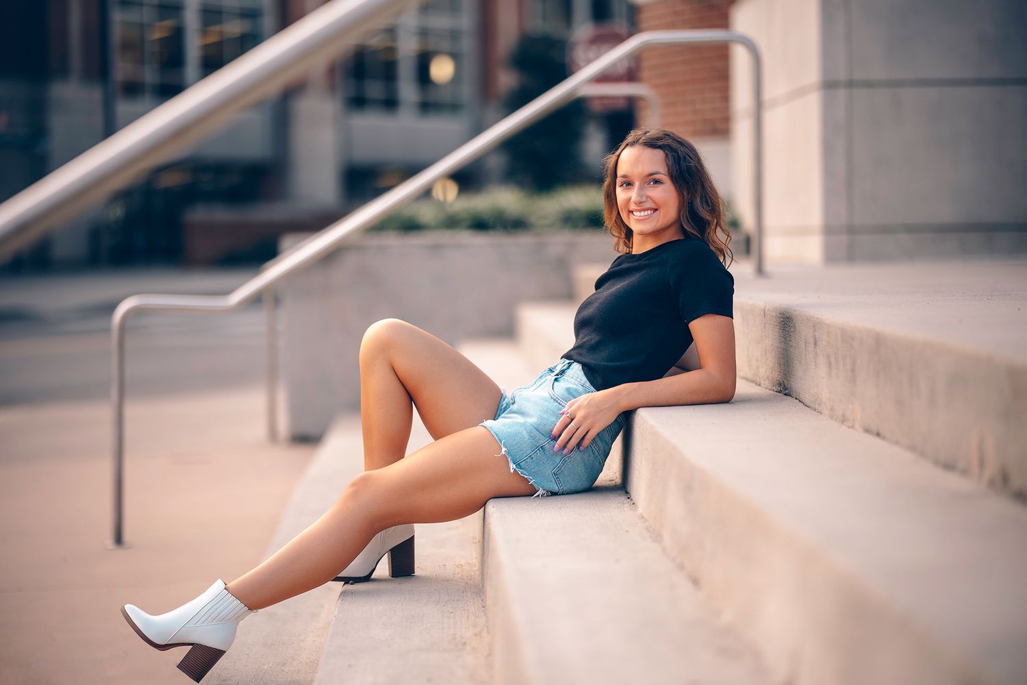 A casual portrait on concrete steps with urban architecture in the background.