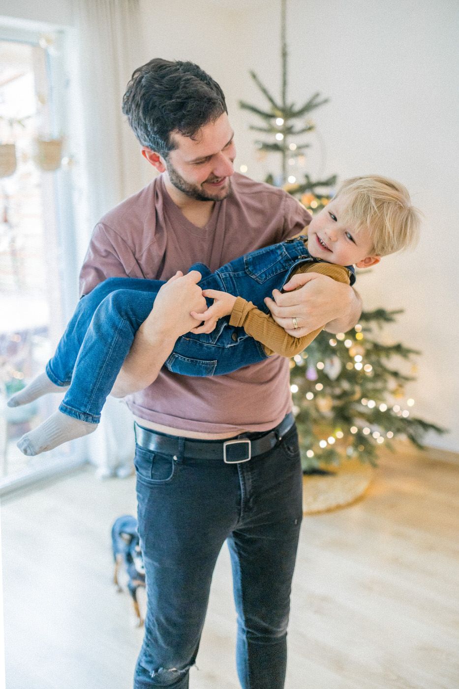 Playful moment between parent and child with Christmas tree in background.