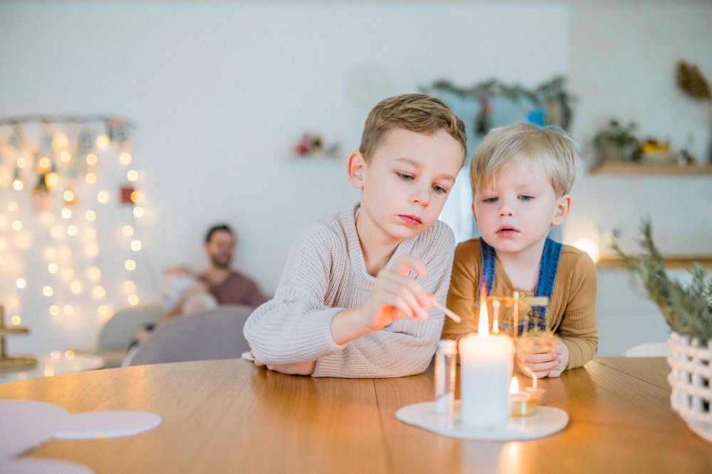 Two children focused intently on lit candle on wooden table.