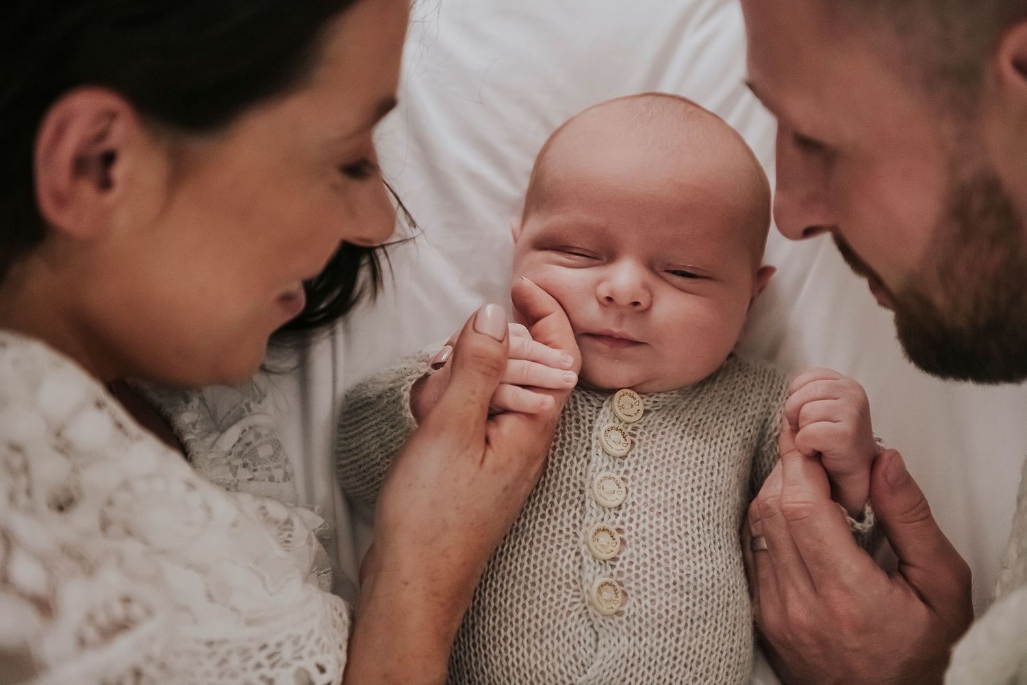 A tender family moment as parents lovingly gaze at their newborn wearing a knit onesie.