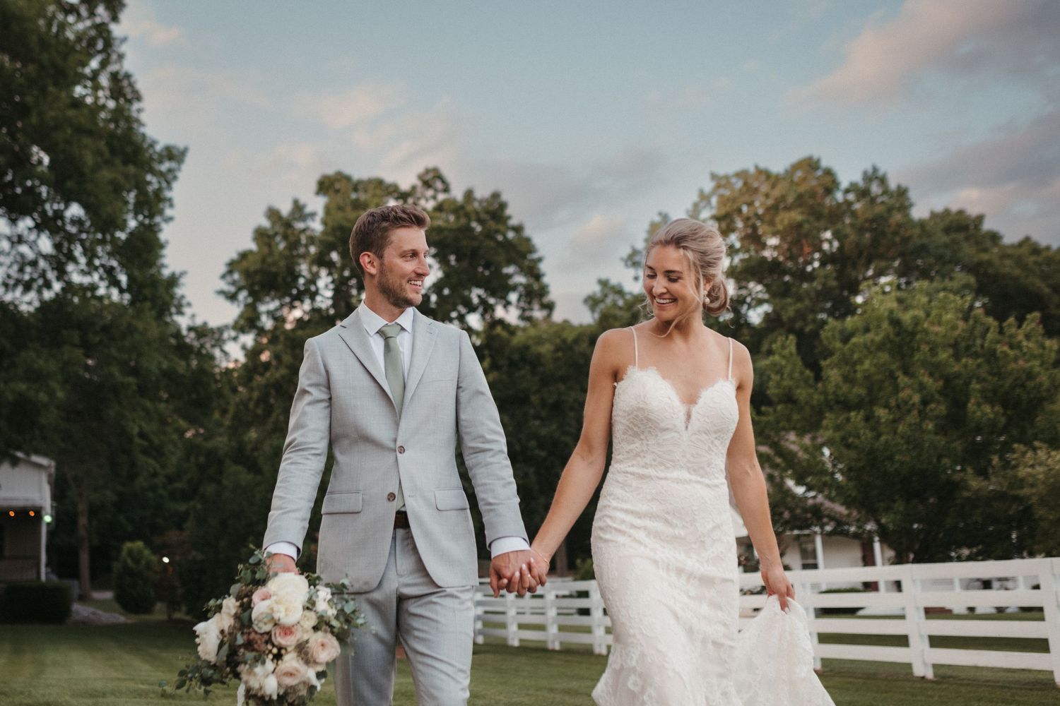 A couple poses together in a rustic outdoor setting with white fences in the background.