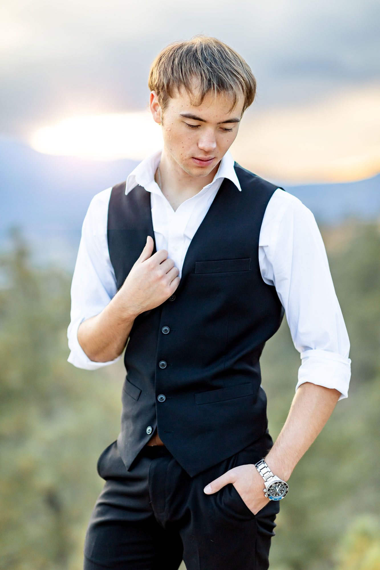 Senior guy gazes downward with one hand in pocket and one on his vest at his senior session at Palmer Park in Colorado.