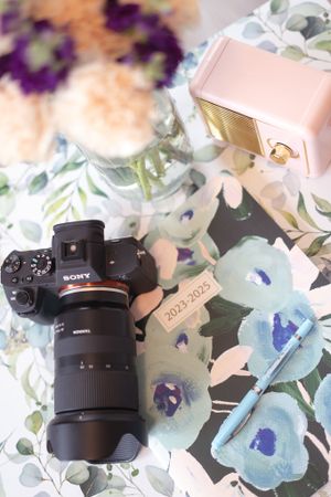 Sony camera with telephoto lens displayed on floral fabric with pink and purple watercolor patterns.