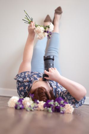 Creative overhead shot of photographer lying on floor with flowers and camera.