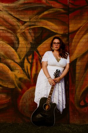 Artistic photo series of a musician in white dress playing acoustic guitar against graffiti wall.