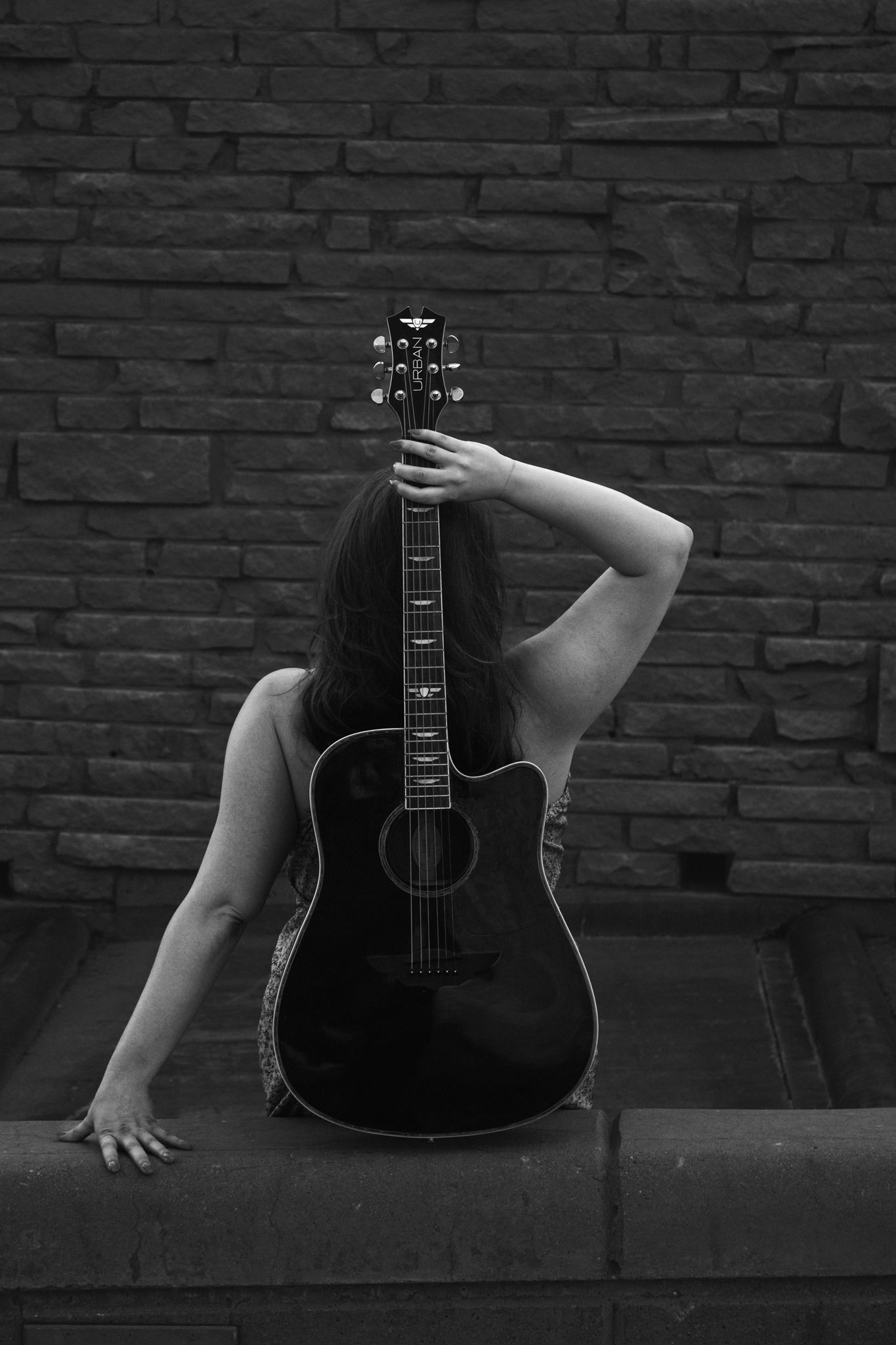 Black and white artistic series showing acoustic guitar against brick wall with dramatic lighting.