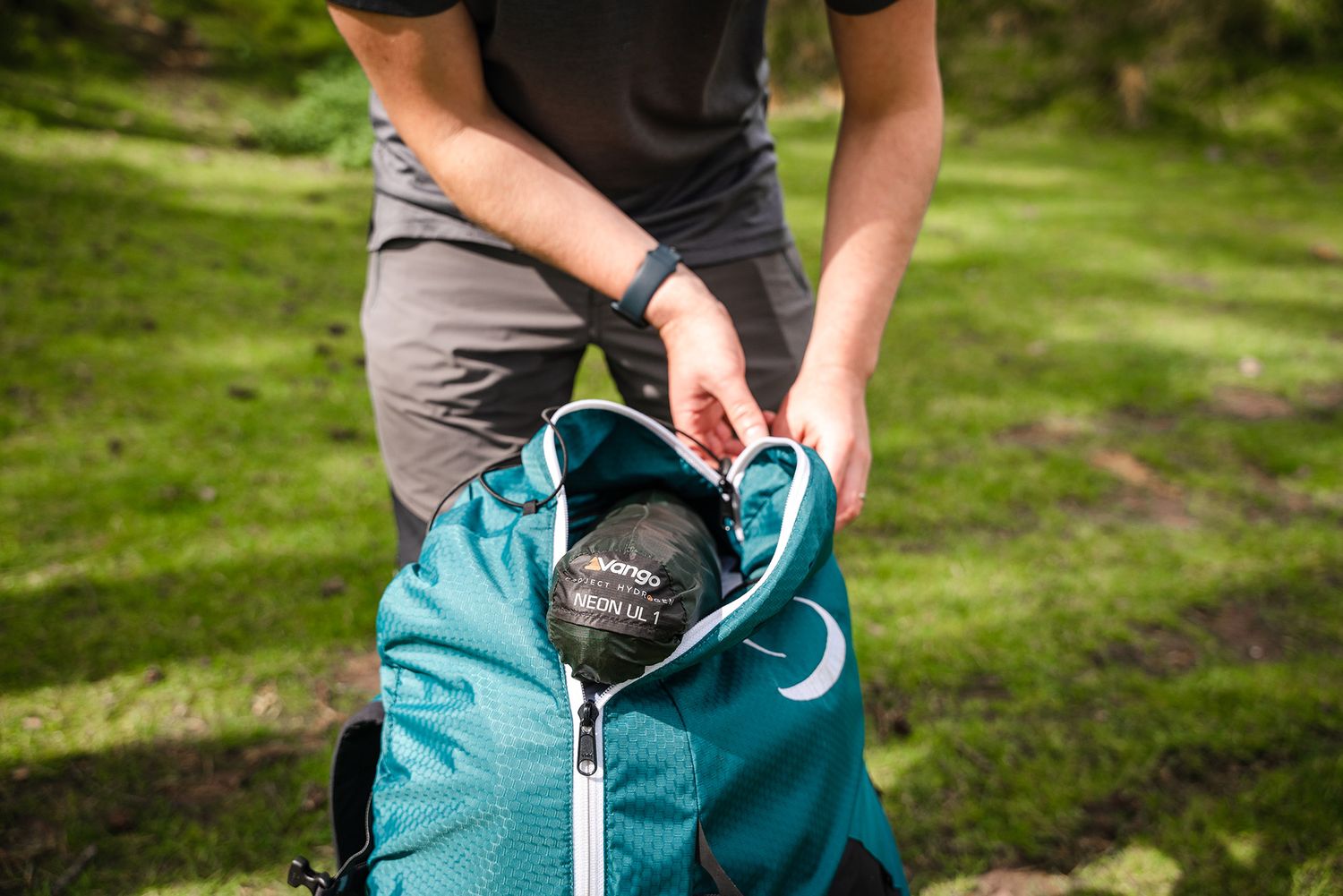 Hands packing a teal colored hiking backpack outdoors.