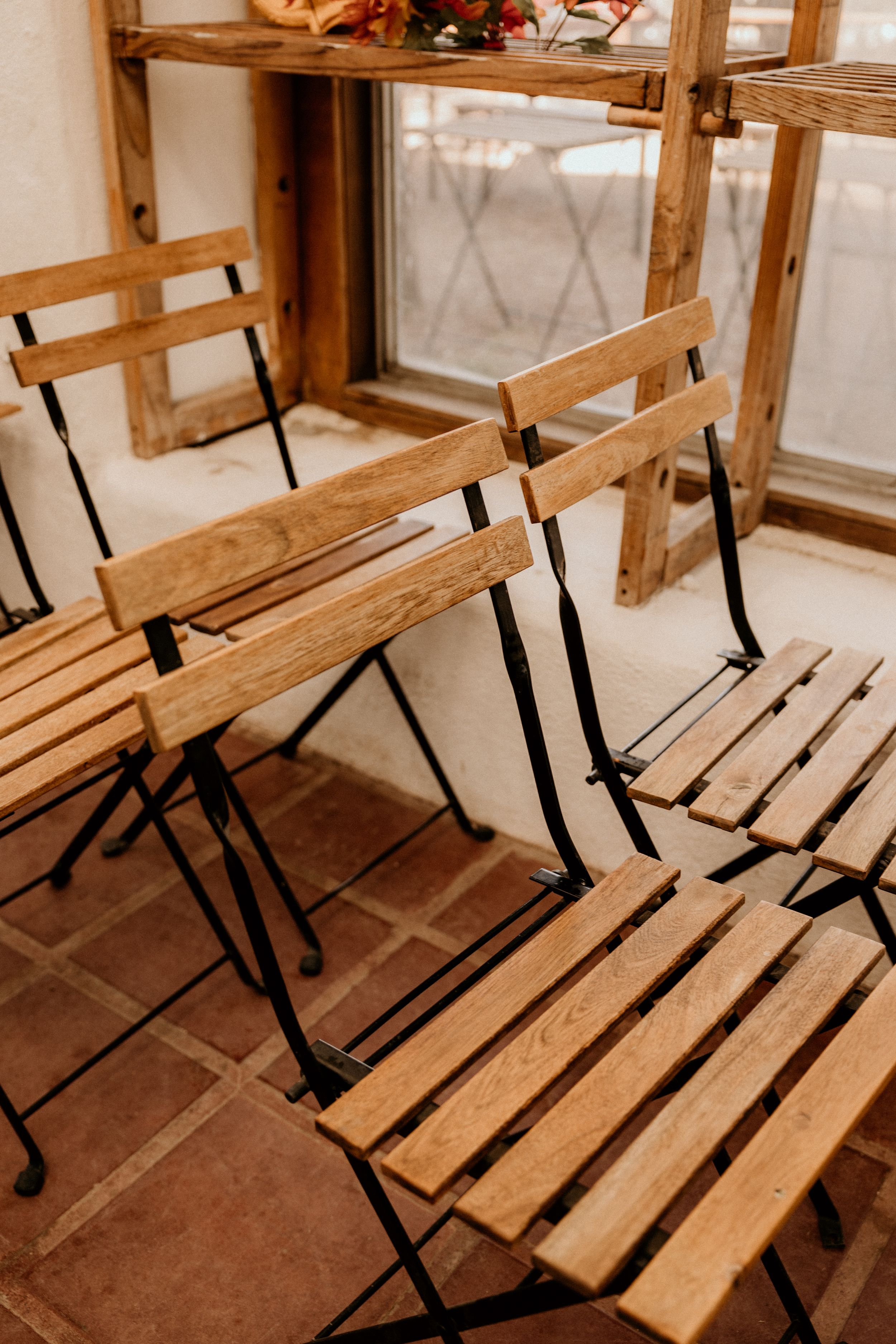 Rows of wooden folding chairs with black metal frames arranged on terracotta tile floor indoors.