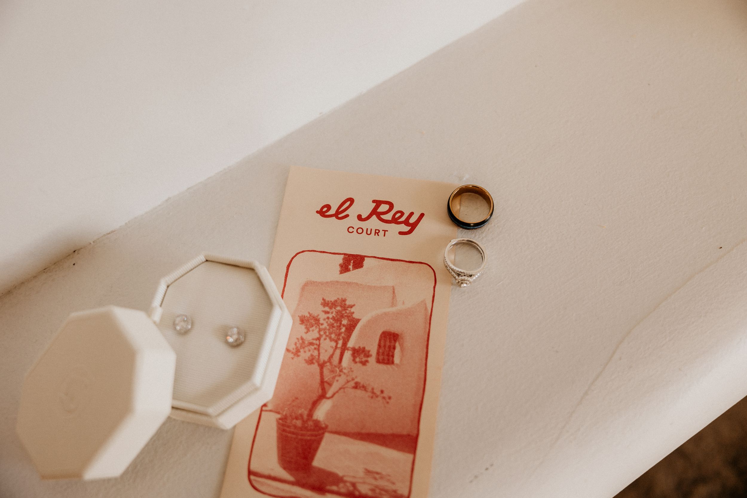 El Rey Court brochure with wedding rings and earrings arranged on white surface as bridal flat lay.