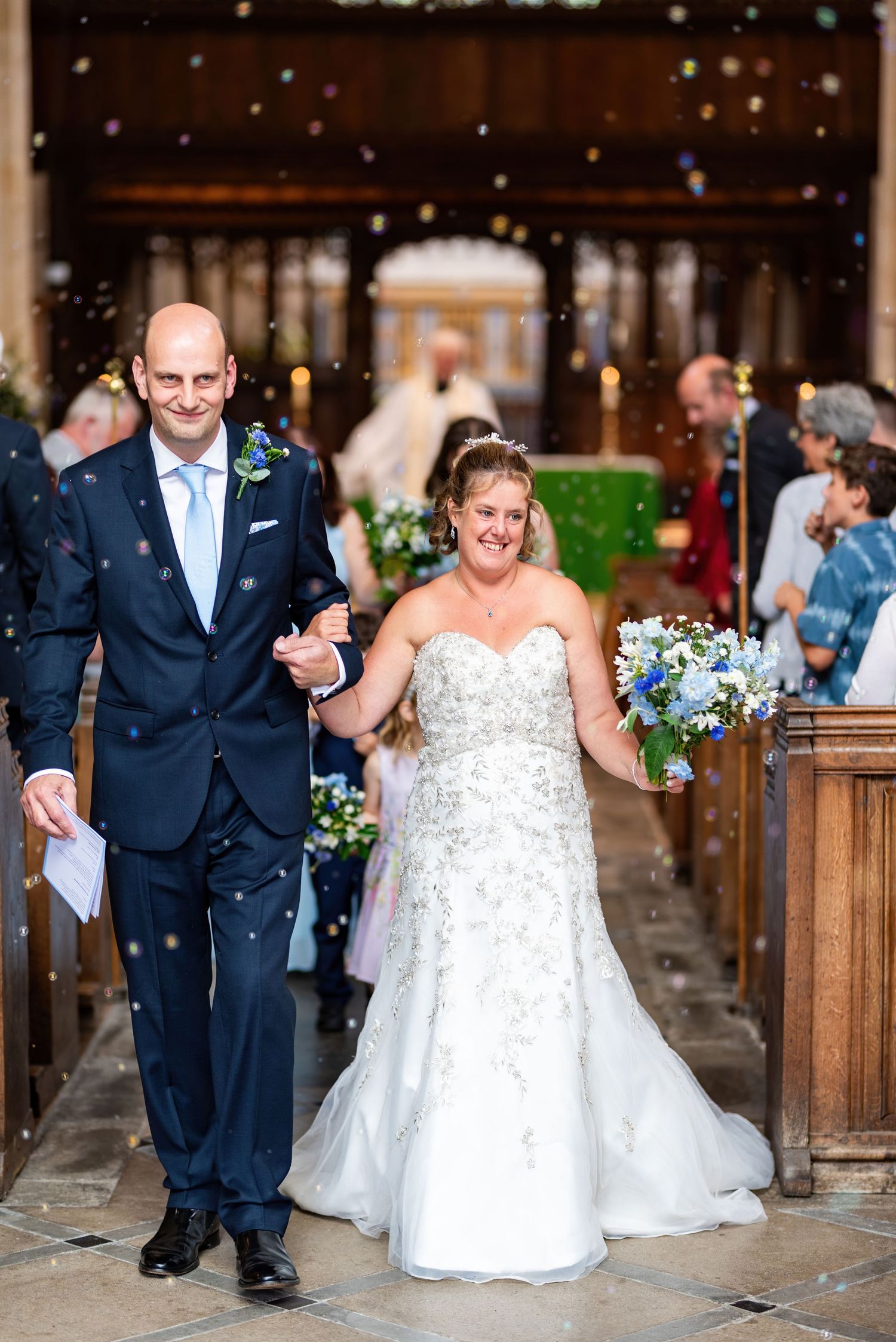 newly weds walking down the isle, bubbles floating in the air. Friends and family smiling