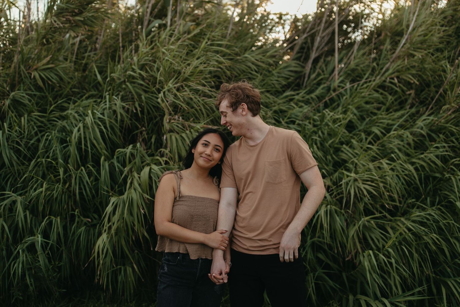 A couple standing together against tall green pampas grass in natural lighting.