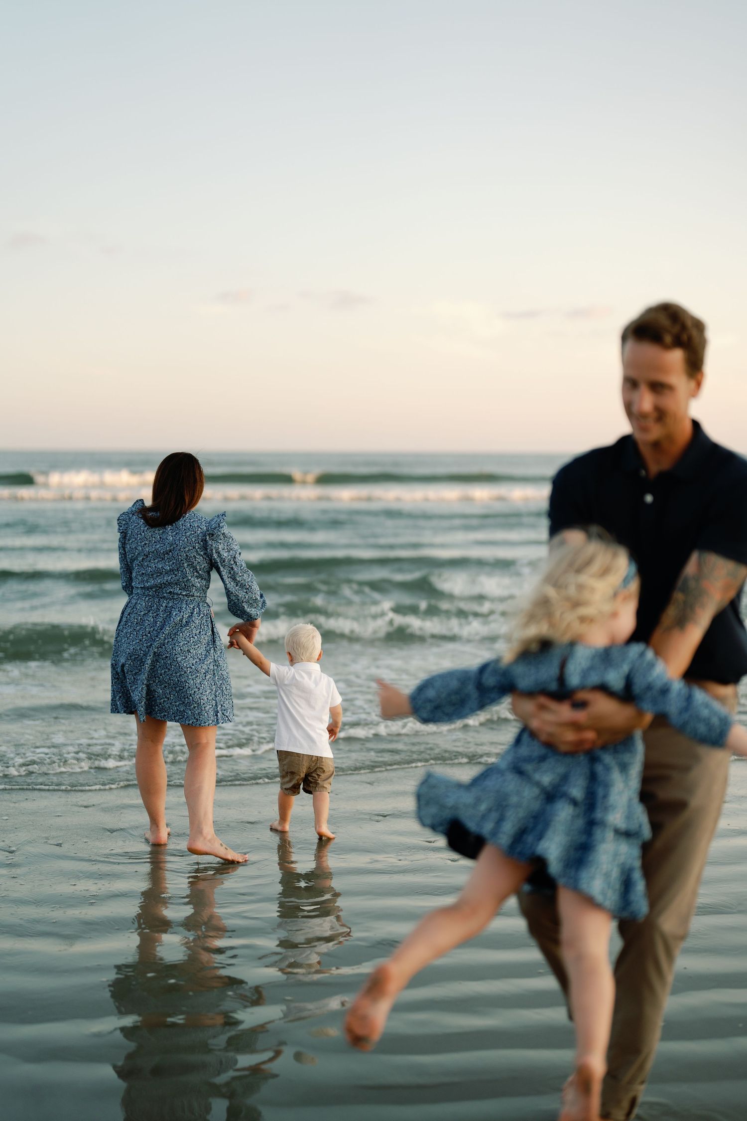 Family of four enjoying a beach walk at sunset with two young children near ocean waves.