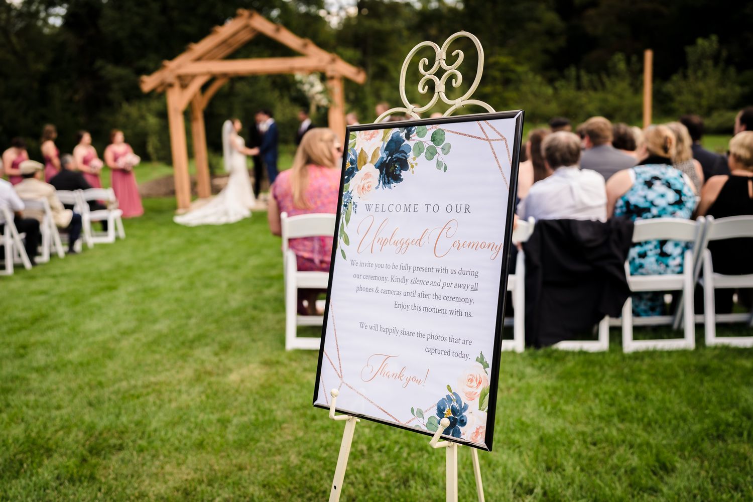 Wedding ceremony signage displayed on stakes in a grassy outdoor venue.