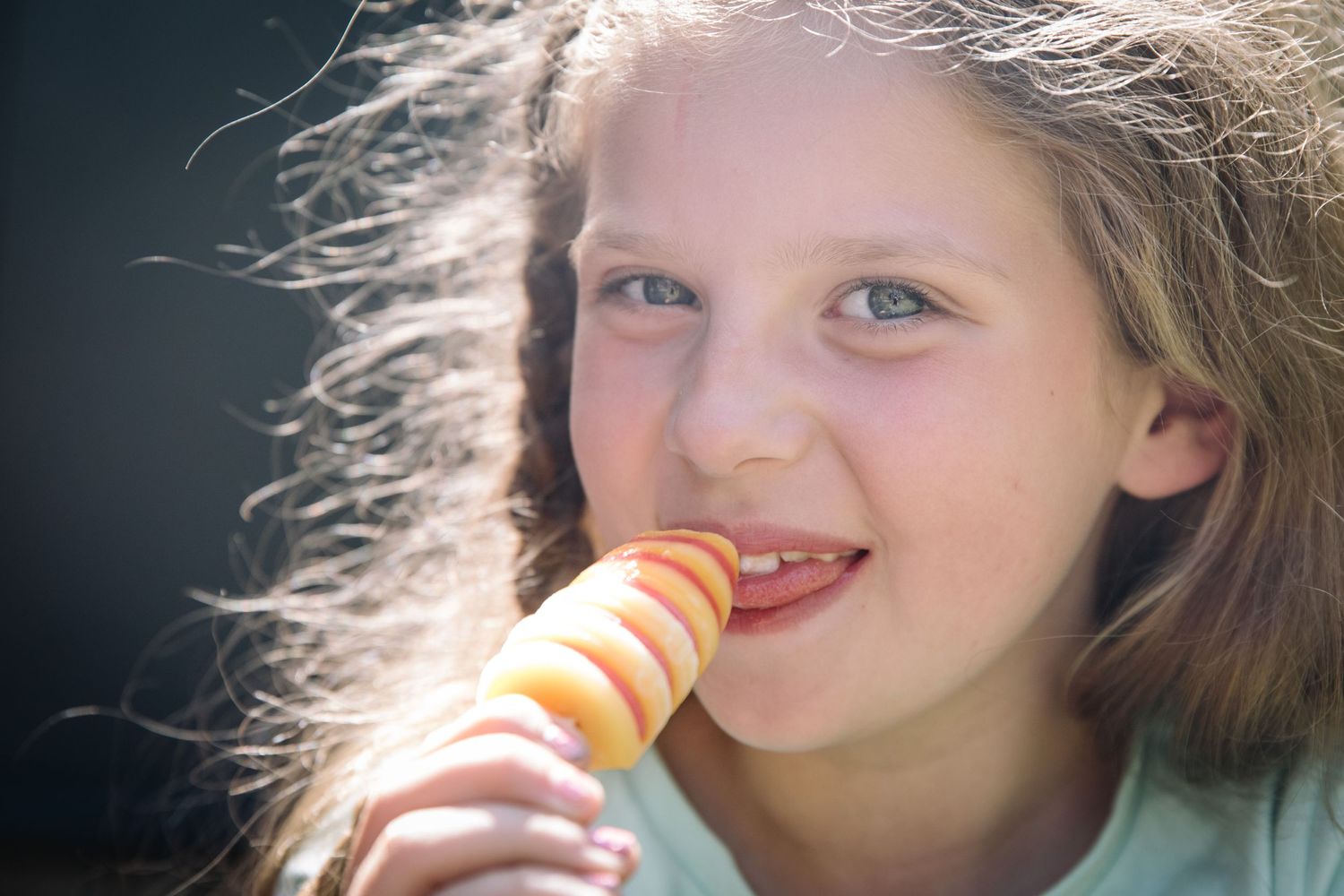 Sun-lit portrait of someone enjoying a striped popsicle on a warm day.