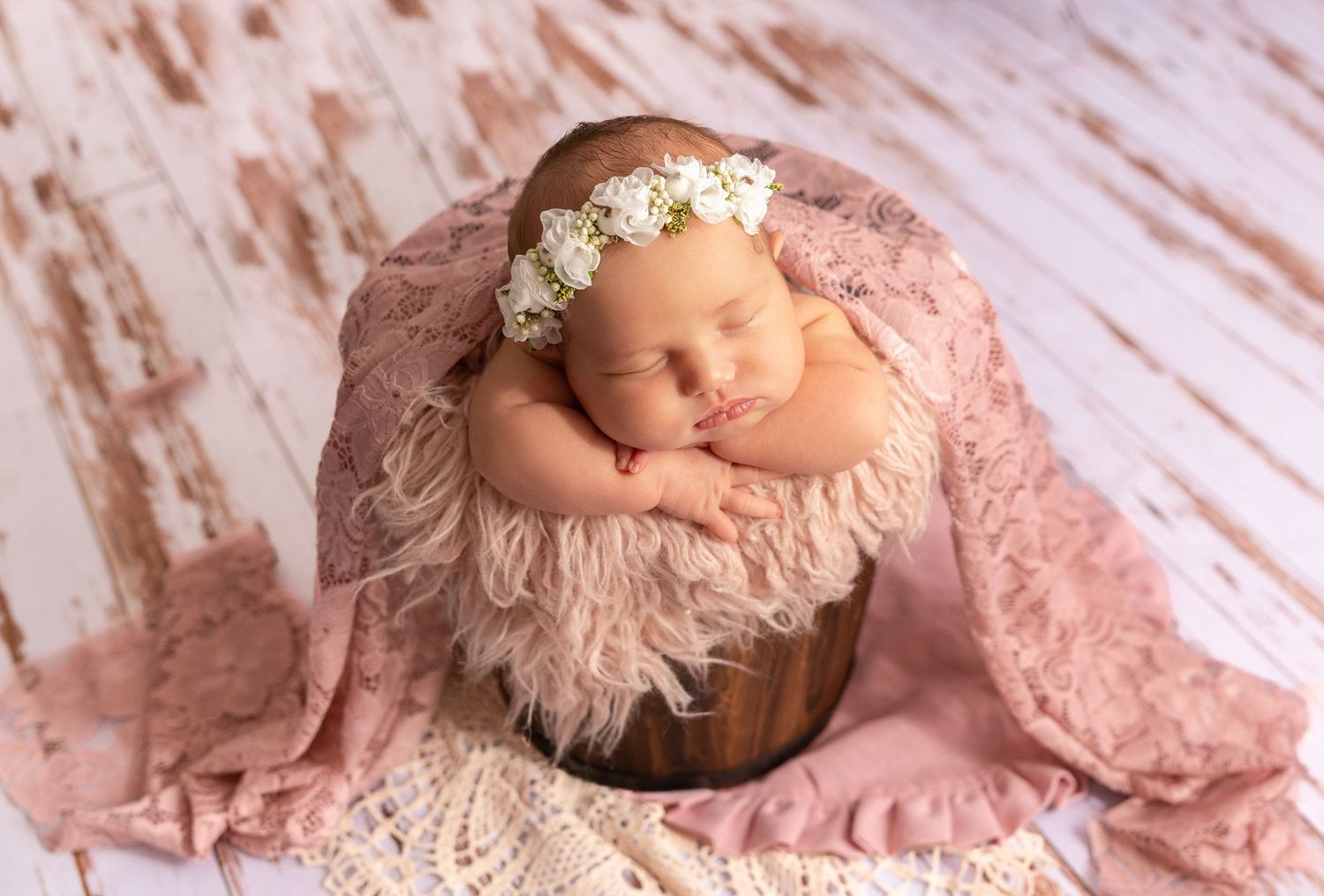 Sleeping newborn with floral headband posed on pink textured backdrop.