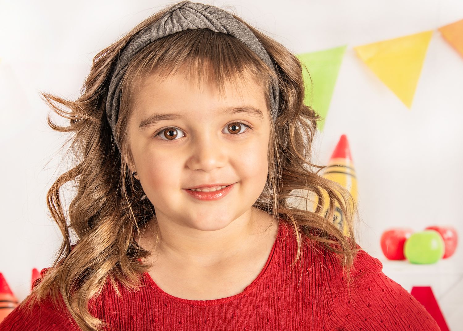 Child wearing red sweater smiles at camera with colorful party bunting decorations in background.