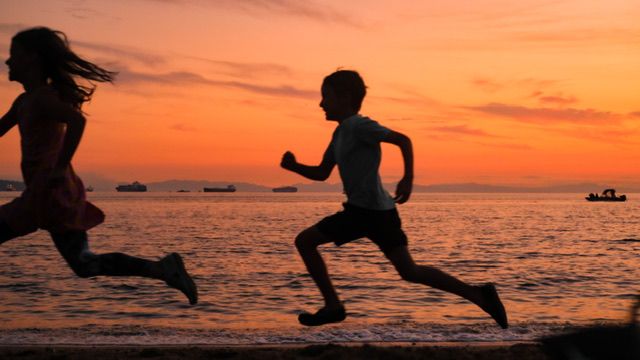 Sunset silhouette of two children racing along Ambleside Beach in West Vancouver